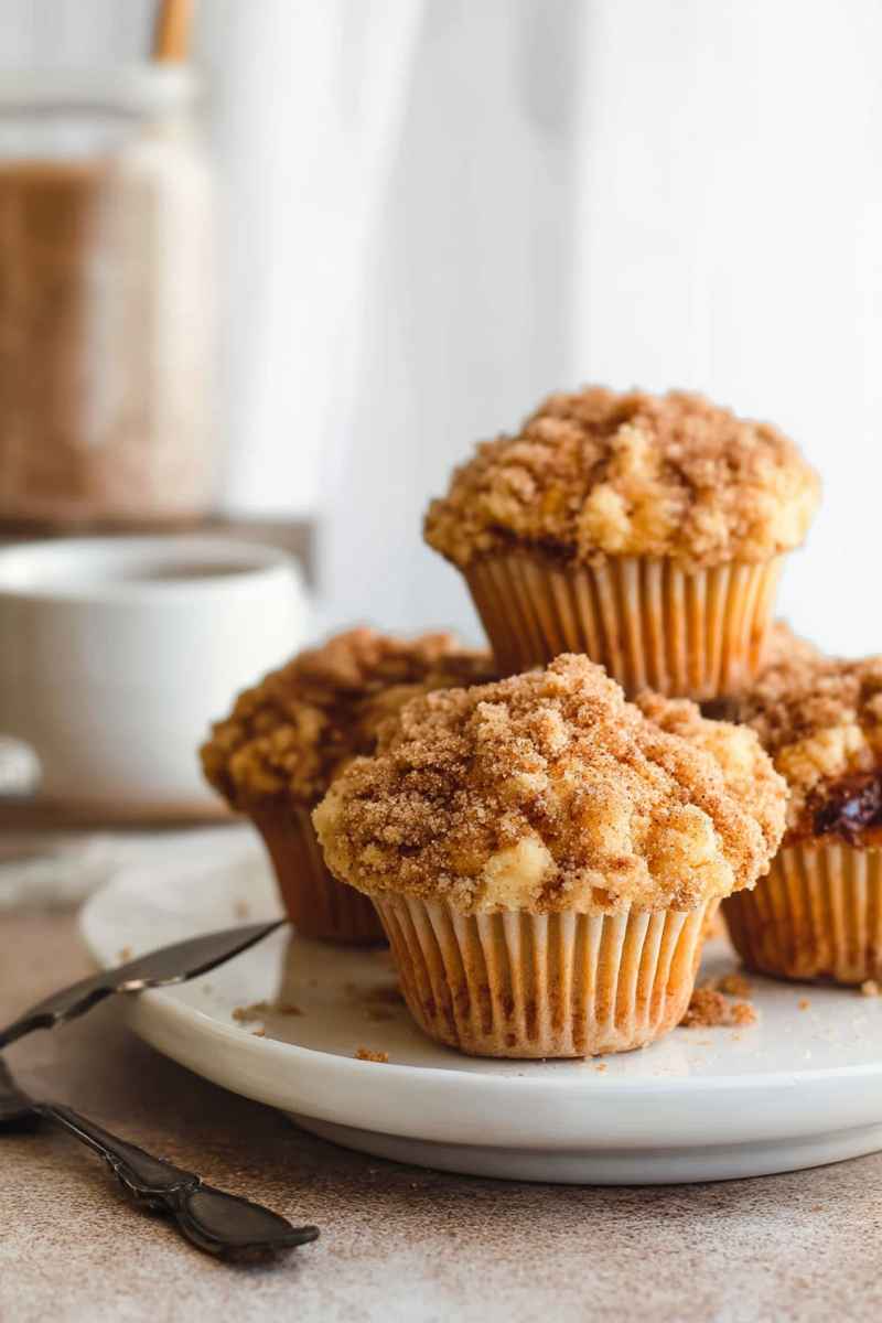 Close-up of golden cinnamon streusel muffins on a white plate, emphasizing their soft texture and crumbly topping.