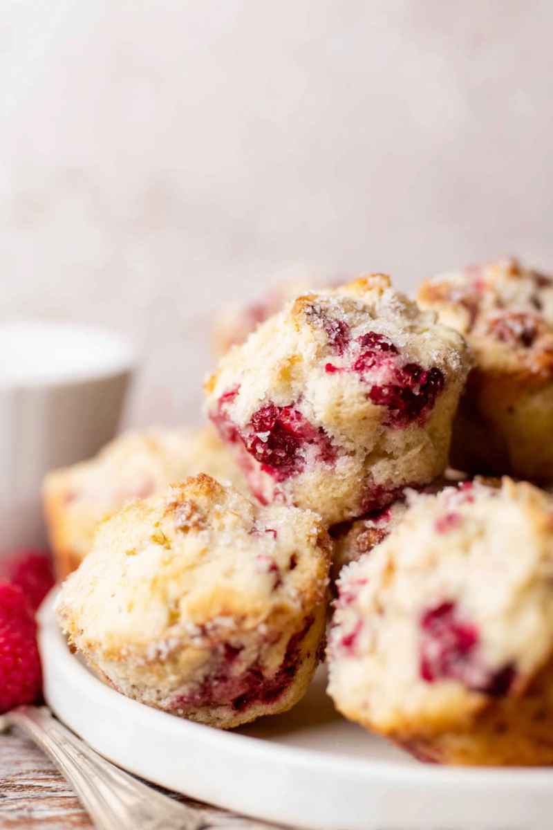 A plate of raspberry muffins dusted with lemon sugar, with one cut open to show the juicy berries inside.