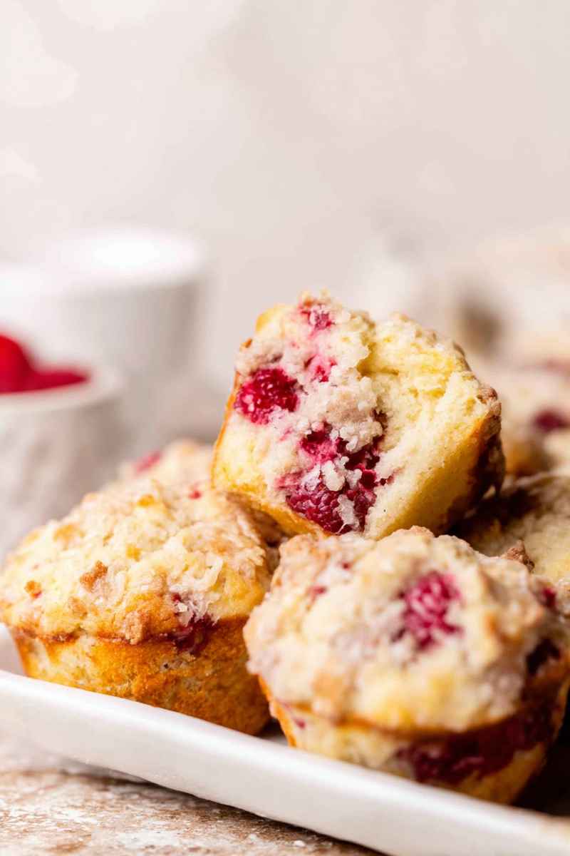 A plate of golden raspberry lemon muffins, with one split open to reveal the juicy berries and moist crumb.