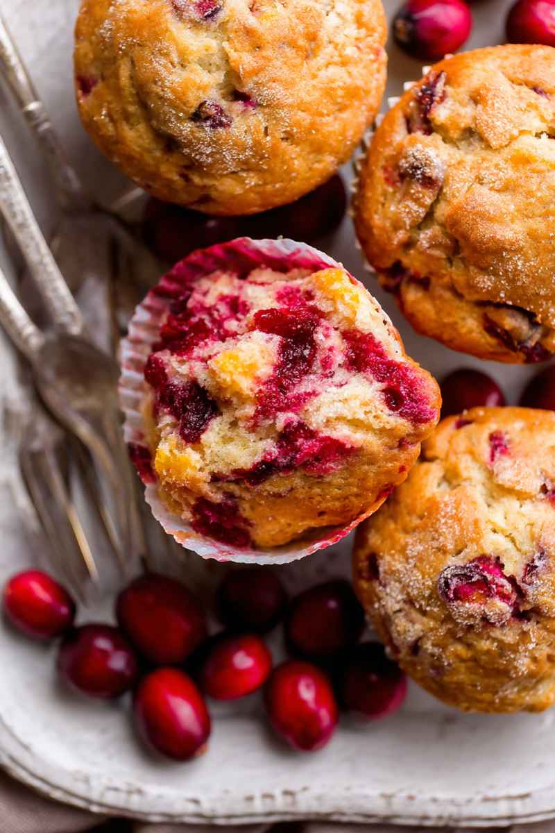Golden Cranberry Orange Muffins topped with sugar, surrounded by fresh cranberries on a rustic plate.
