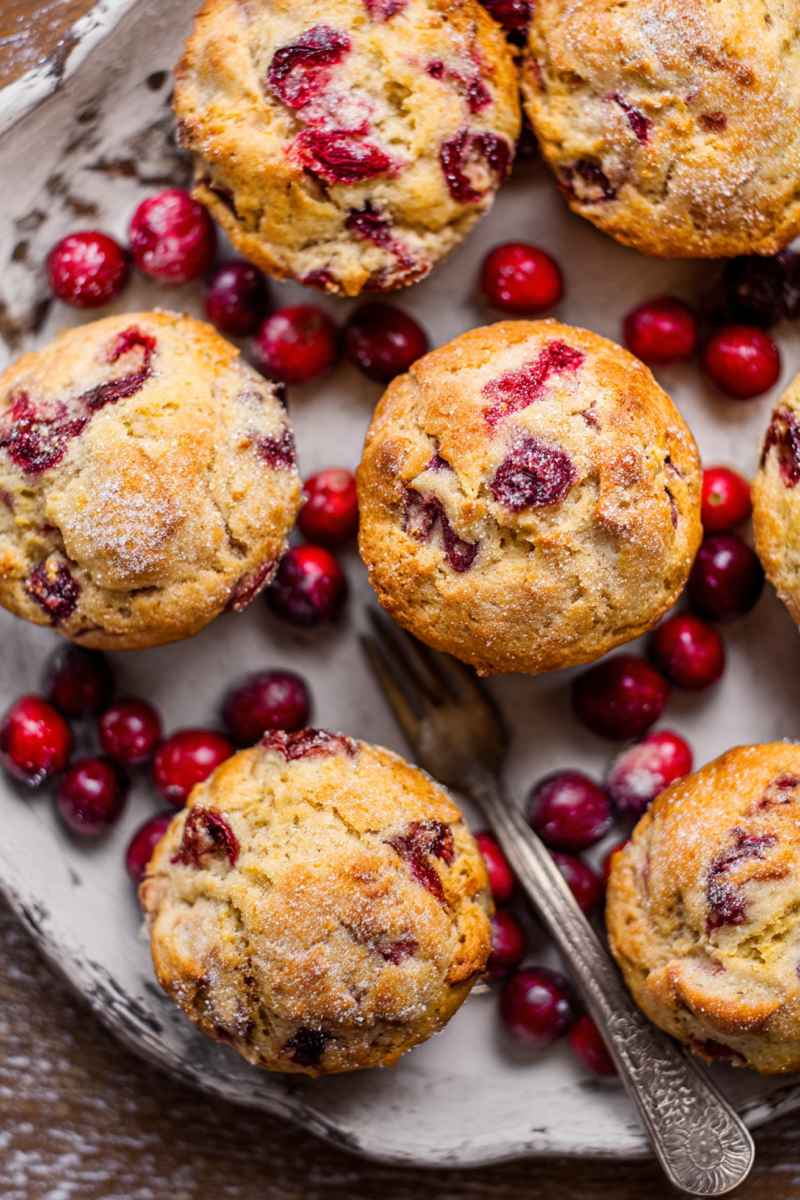Golden Cranberry Orange Muffins with fresh cranberries scattered around, served on a rustic plate.