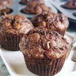 Fluffy chocolate muffins with embedded chocolate chips, displayed on a white platter.