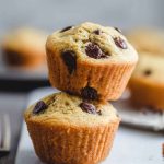 Two orange chocolate chip muffins stacked on a white marble board, emphasizing their fluffy texture and scattered chocolate chips.