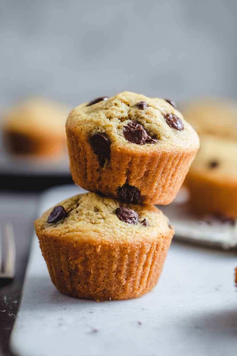 Two orange chocolate chip muffins stacked on a white marble board, emphasizing their fluffy texture and scattered chocolate chips.