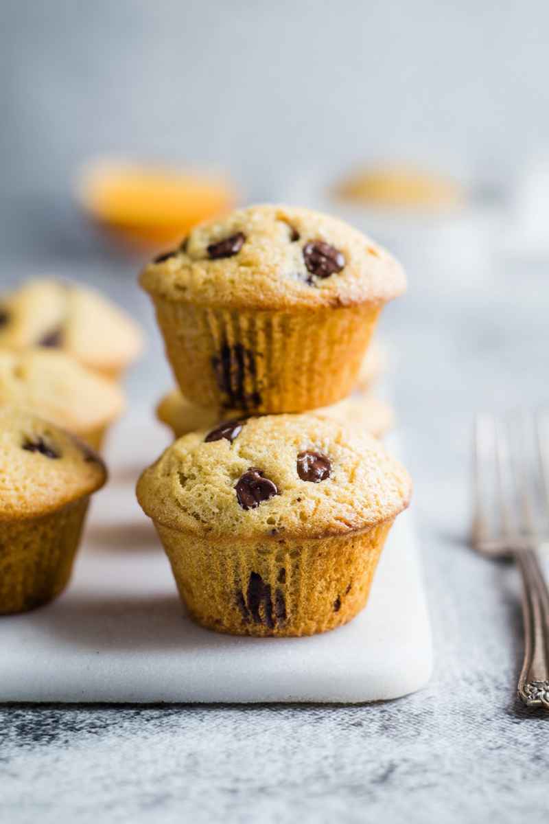 Golden-brown orange chocolate chip muffins stacked on a white marble board, showcasing their soft texture and rich chocolate chips.