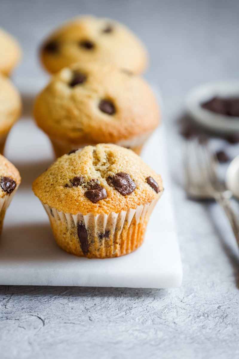 Close-up of an orange chocolate chip muffin on a white marble surface, highlighting its golden texture and embedded chocolate chips.