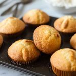 A tray of freshly baked golden vanilla muffins in paper liners, ready to be enjoyed.