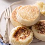 A close-up of golden-brown English muffins stacked on a plate, showcasing their crispy texture and inviting appearance.