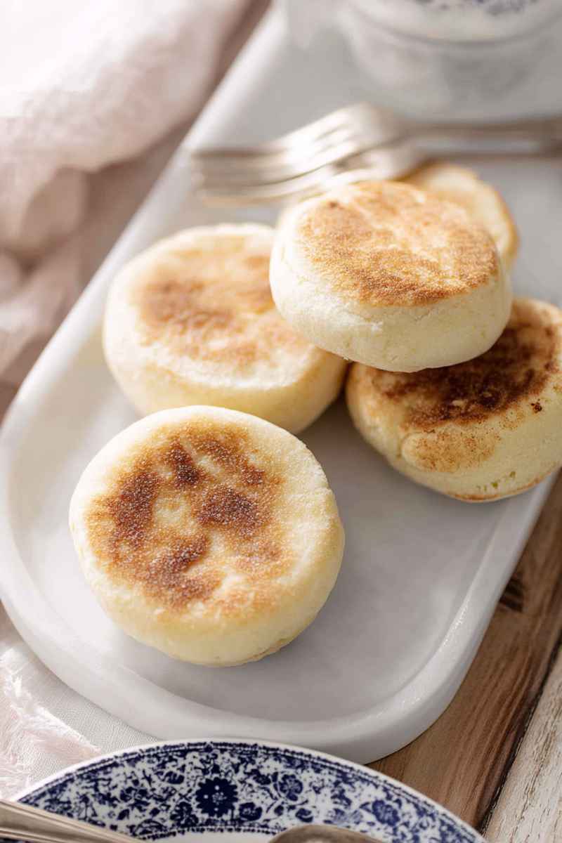 A plate of freshly baked English muffins, neatly stacked and ready to be served, with a blue-and-white patterned napkin underneath.