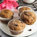 Espresso Chocolate Chip Muffins dusted with powdered sugar, surrounded by chocolate chips and pink flowers.