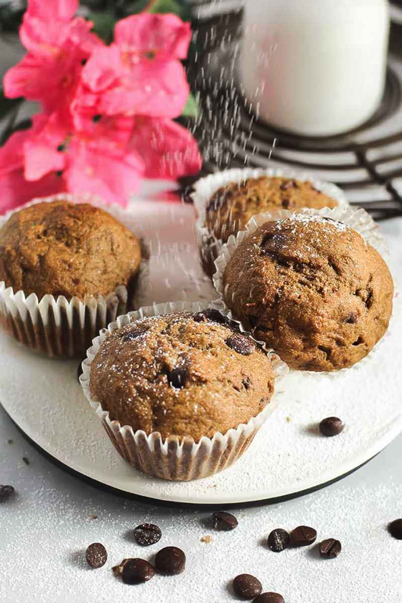 Espresso Chocolate Chip Muffins dusted with powdered sugar, surrounded by chocolate chips and pink flowers.