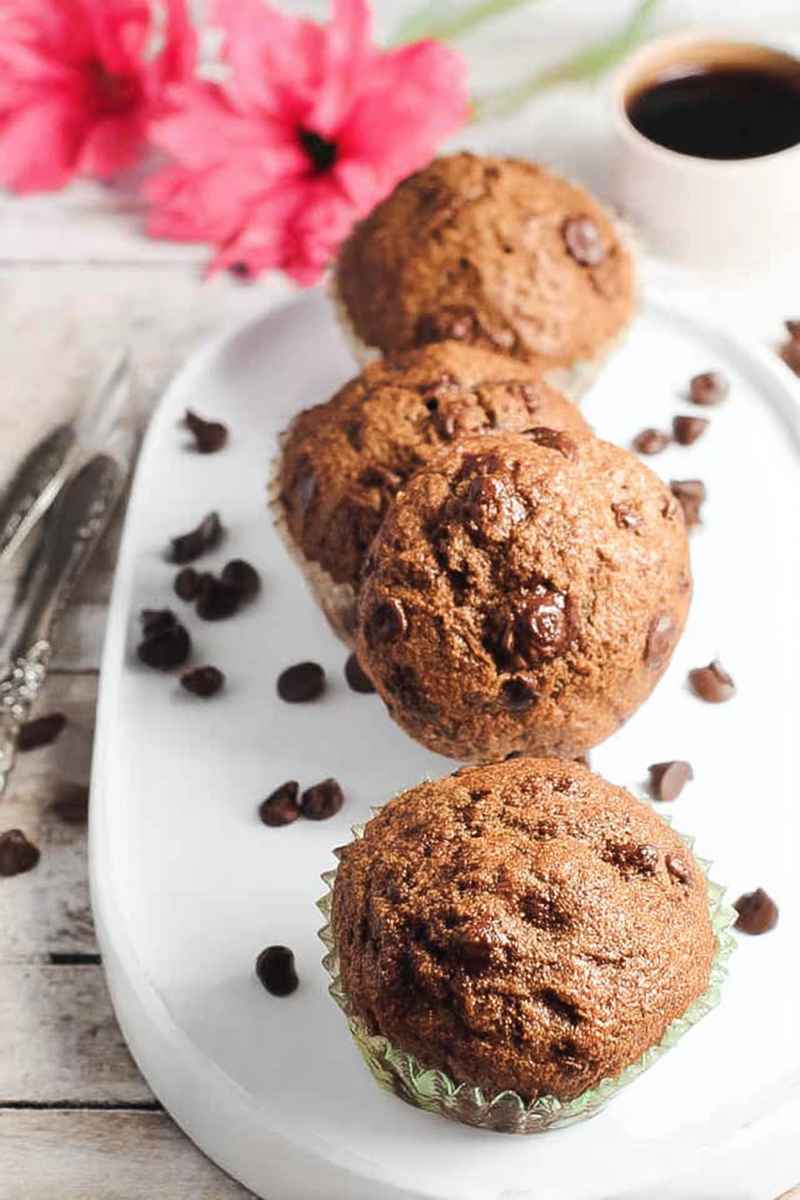 Delicious Espresso Chocolate Chip Muffins on a white plate, surrounded by scattered chocolate chips and vibrant pink flowers.