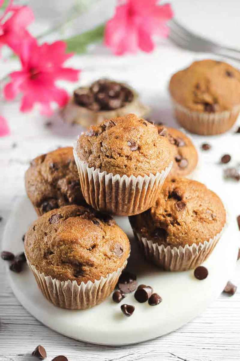 Stacked Espresso Chocolate Chip Muffins on a white plate, garnished with chocolate chips and bright pink flowers.