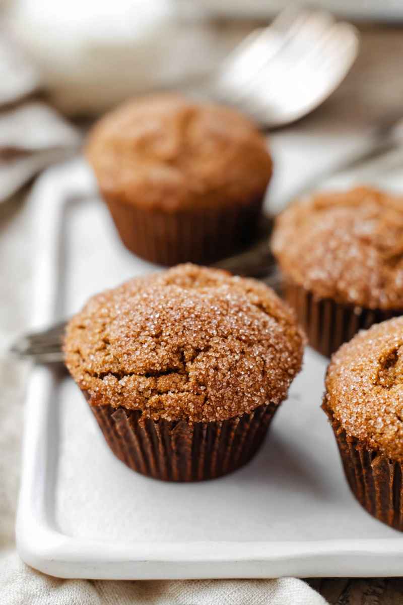 Golden gingerbread muffins dusted with sparkling sugar, presented on a white tray with a cozy background.