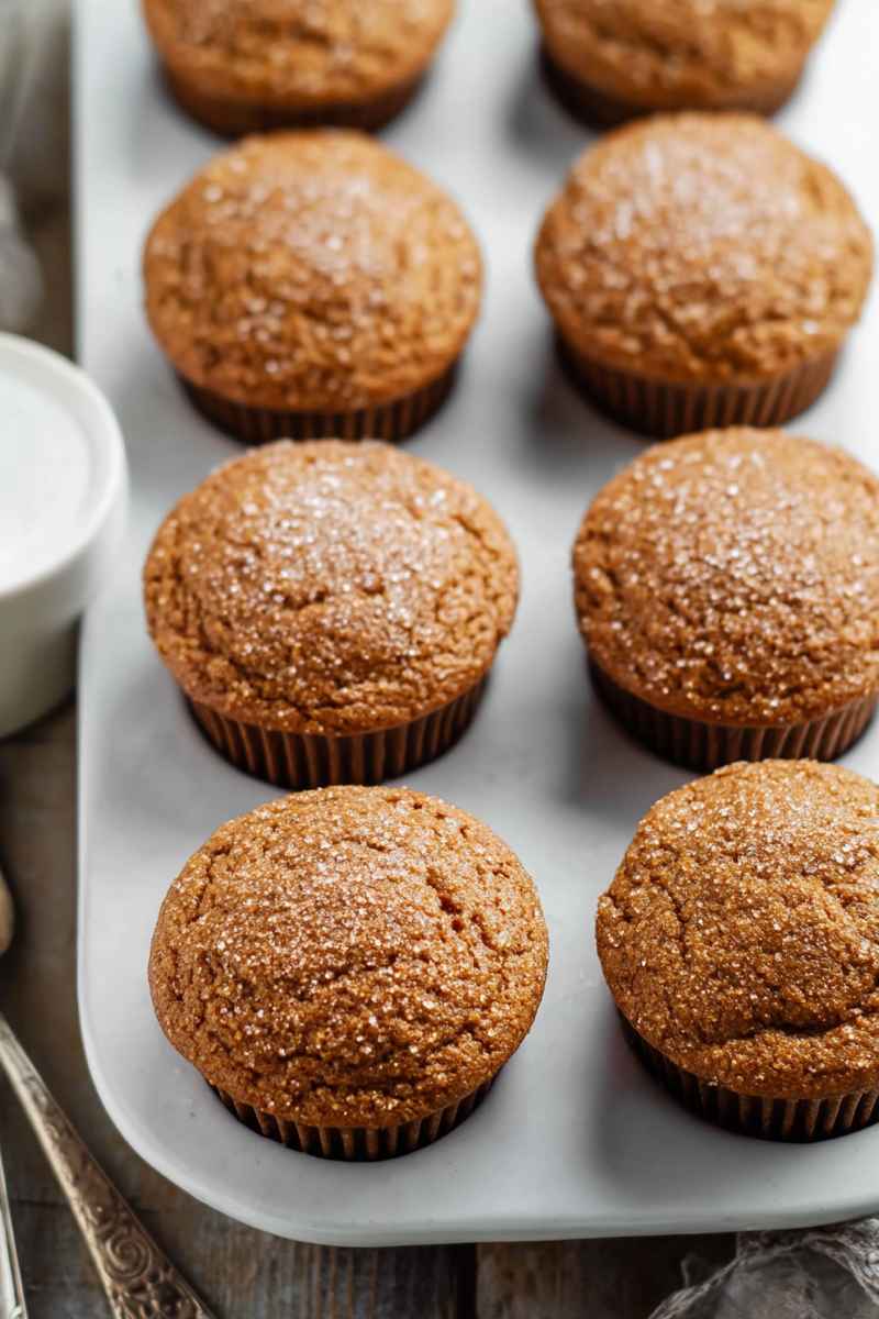 Six golden-brown gingerbread muffins dusted with sparkling sugar, arranged on a white tray, ready to be enjoyed.