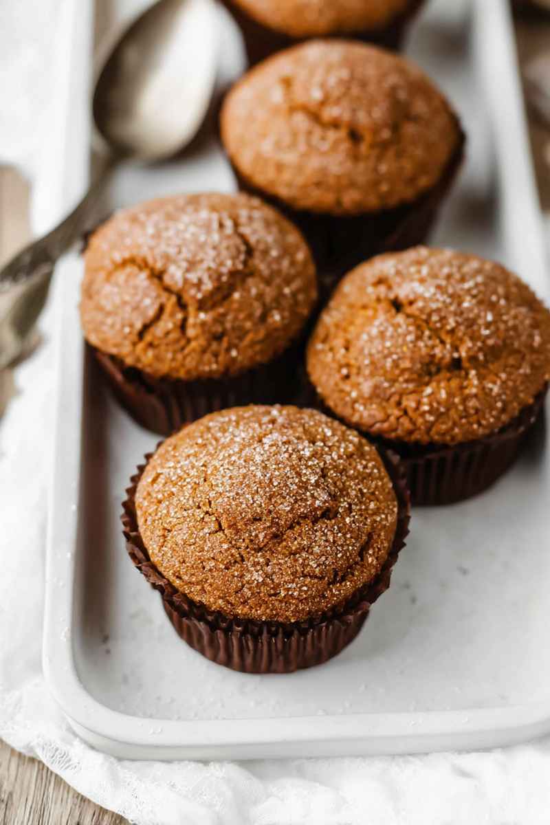 Delicious gingerbread muffins topped with sparkling sugar, served on a white tray with a vintage spoon nearby.