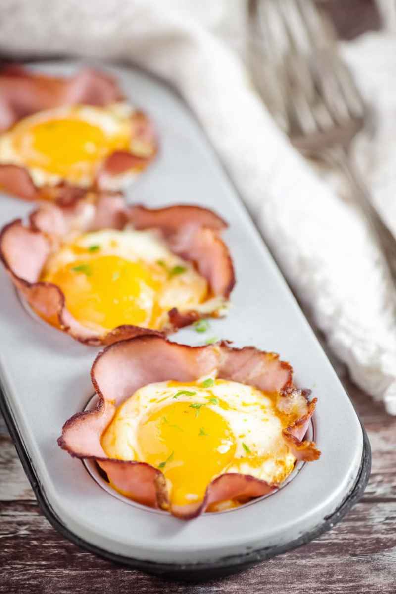 Golden egg yolks nestled in crispy ham cups on a white rectangular plate.
