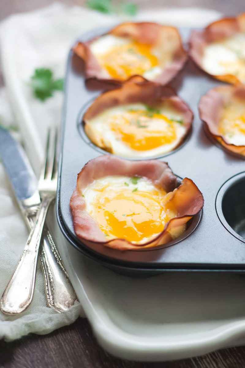 Baked egg cups in a muffin tin lined with ham slices, ready to serve.