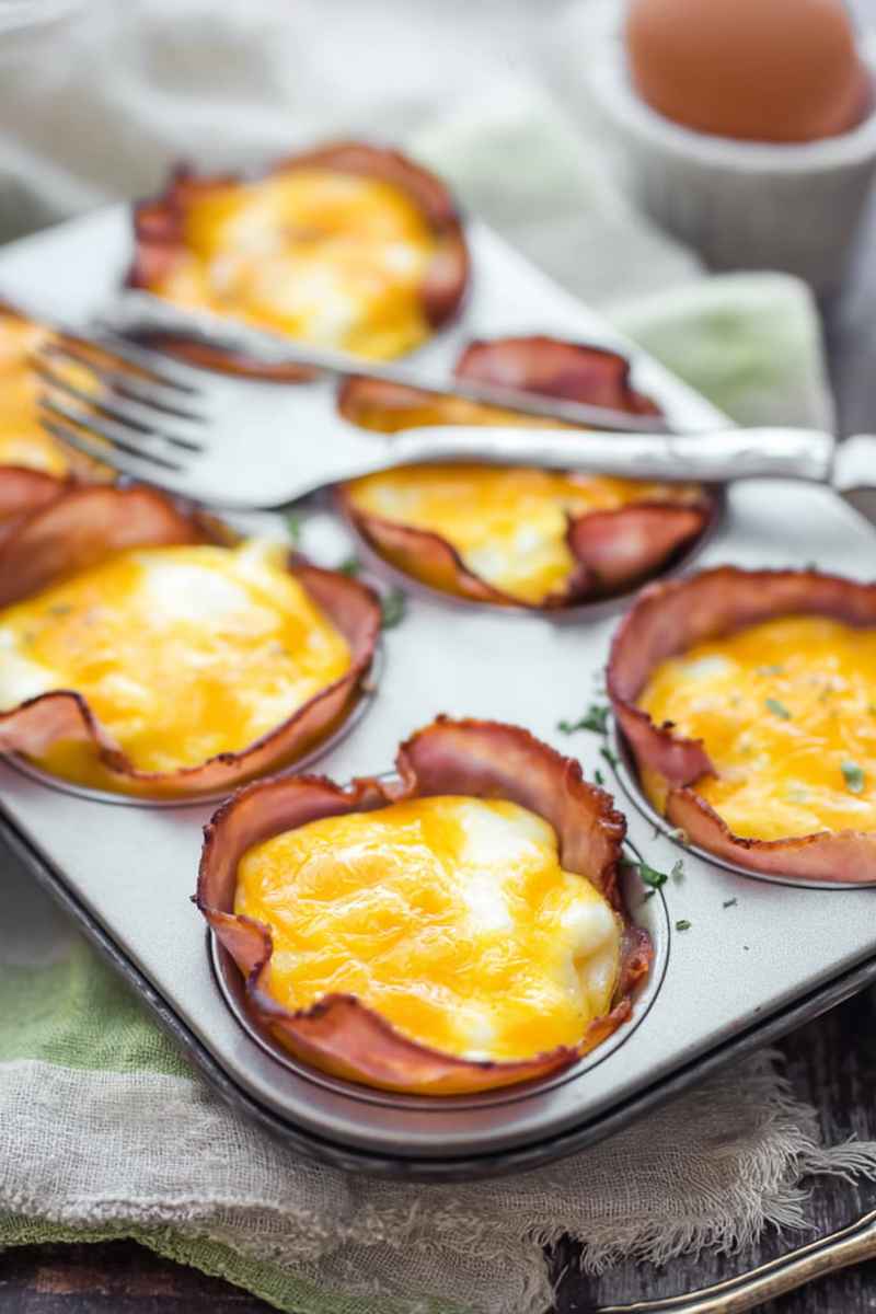 Baked egg cups with golden yolks, wrapped in crispy ham slices, arranged on a white serving tray.