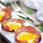 Golden-brown baked egg cups nestled in crispy ham slices on a white serving tray.