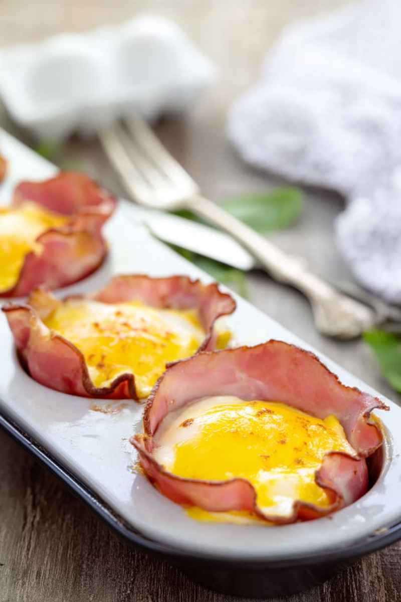 Golden-brown baked egg cups nestled in crispy ham slices on a white serving tray.
