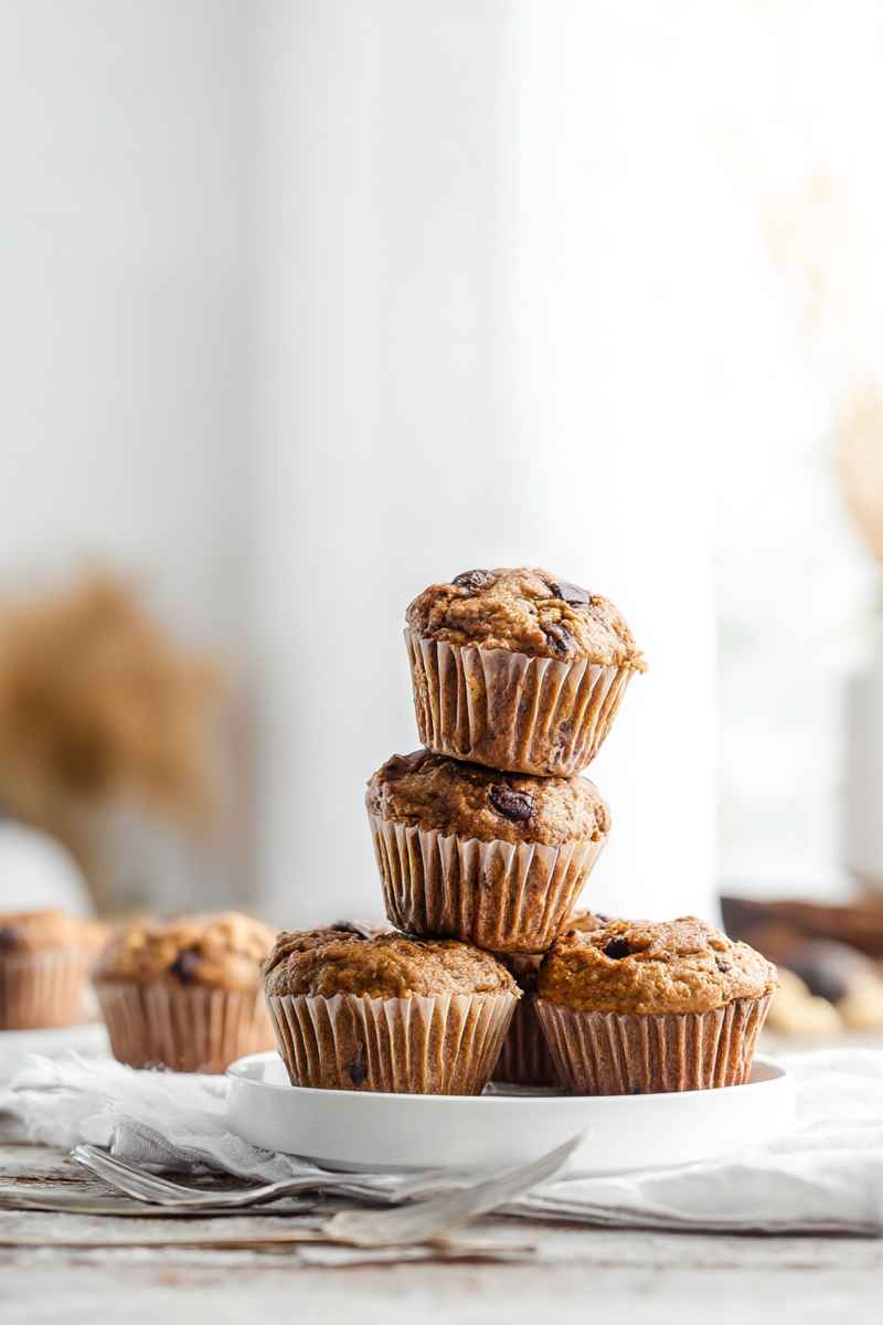 Golden Peanut Butter Banana Muffins stacked on a white plate, featuring dark chocolate chips.