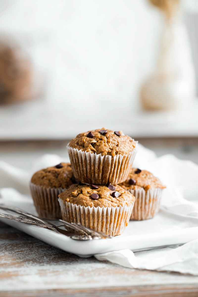 Peanut Butter Banana Muffins stacked on a white plate, featuring golden-brown tops and dark chocolate chips.
