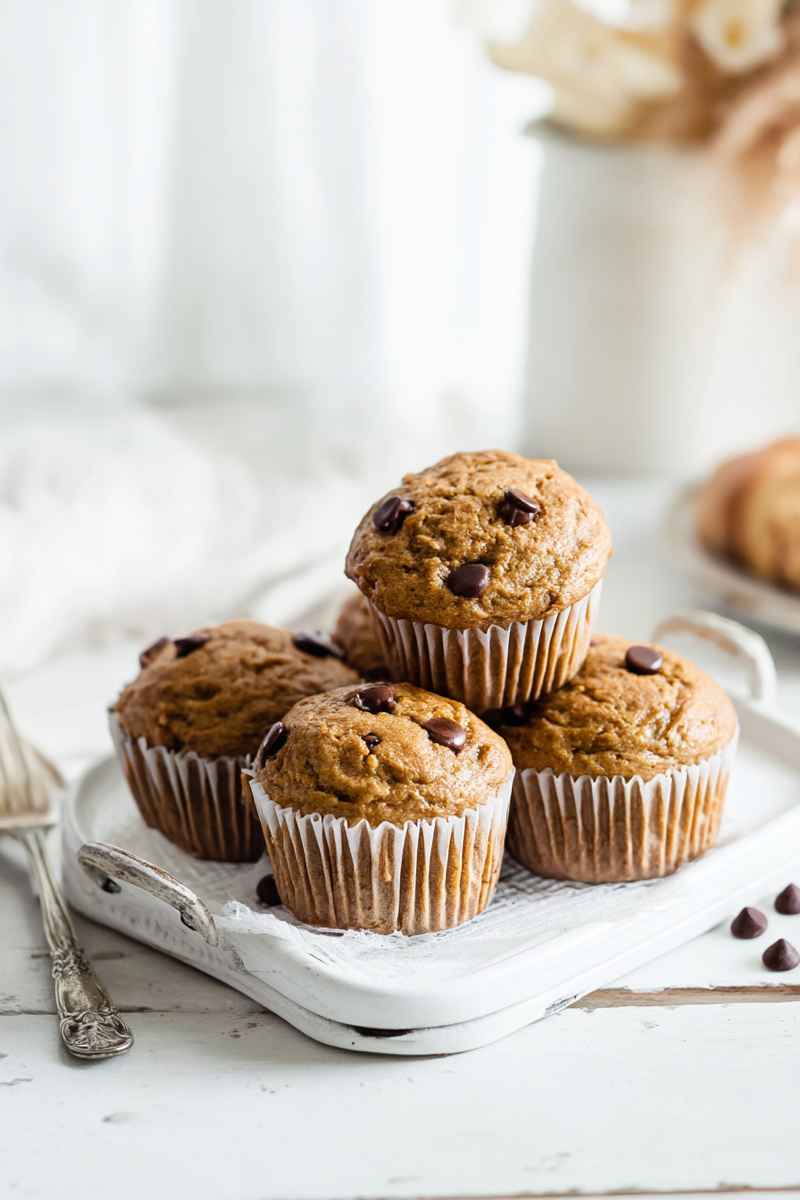 Stacked Peanut Butter Banana Muffins with visible dark chocolate chips on a rustic wooden table.