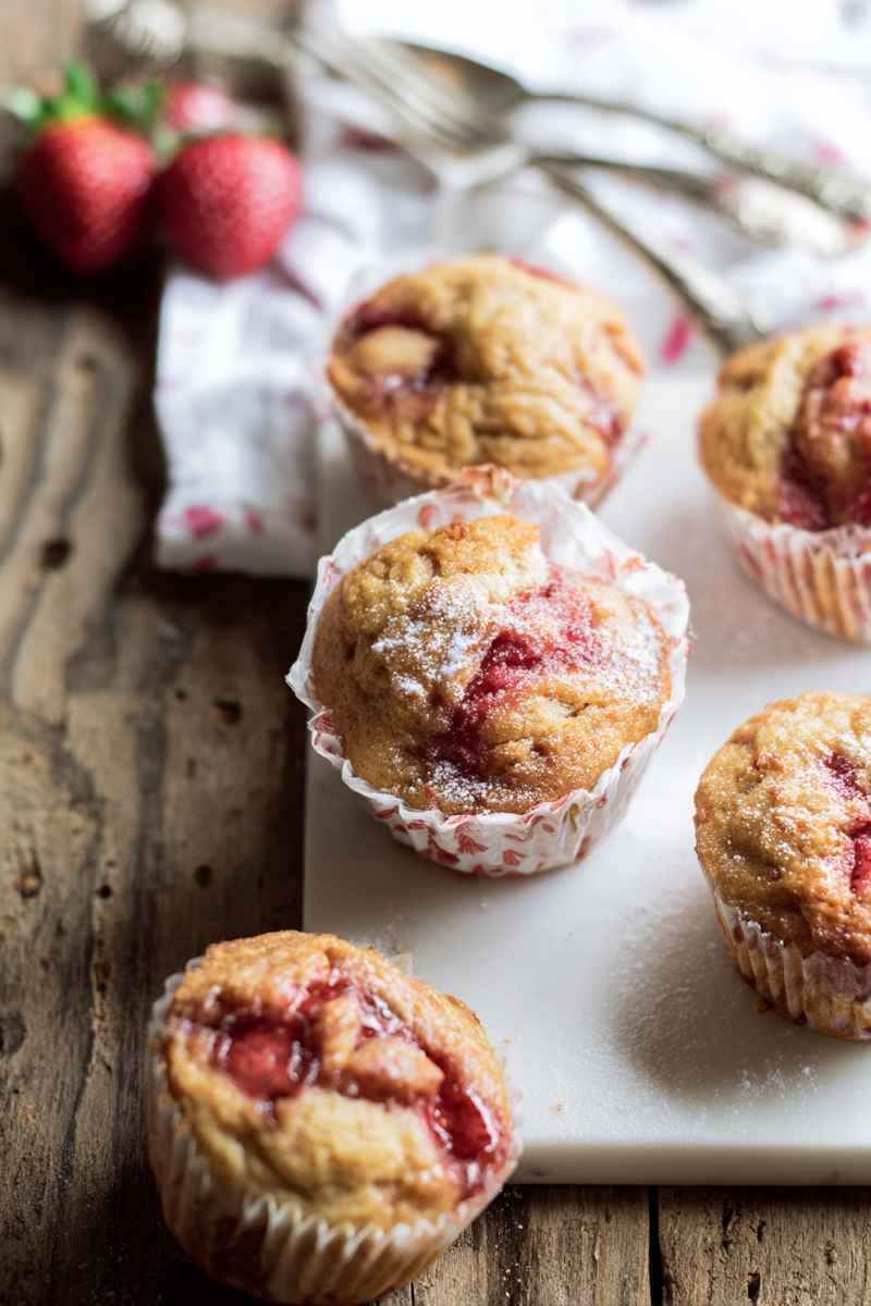 Fluffy Honey Strawberry Muffins with visible strawberry chunks, dusted with powdered sugar, displayed on a white marble tray.