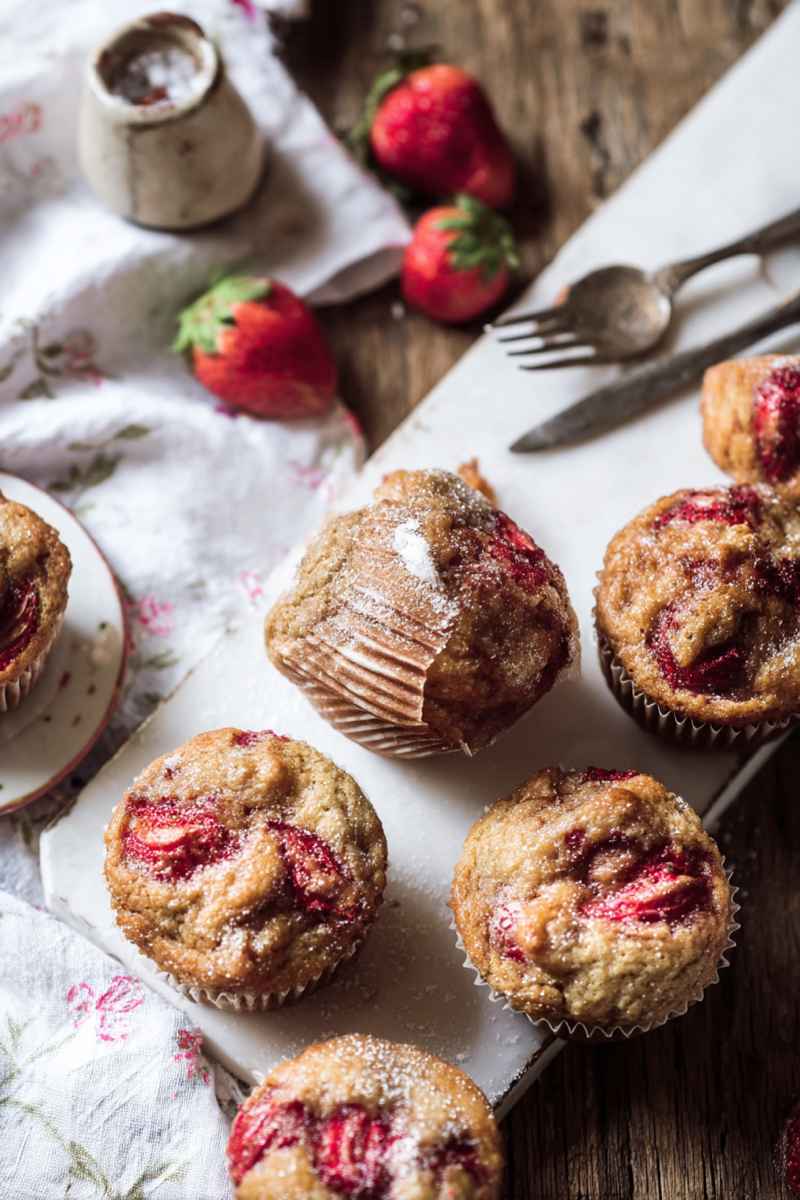 Golden Honey Strawberry Muffins with bright red strawberry swirls, placed on a marble surface with fresh strawberries in the background.