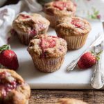 Golden-brown Honey Strawberry Muffins with juicy strawberry swirls, served on a marble board with fresh strawberries.