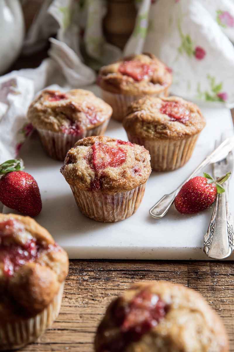Golden-brown Honey Strawberry Muffins with juicy strawberry swirls, served on a marble board with fresh strawberries.
