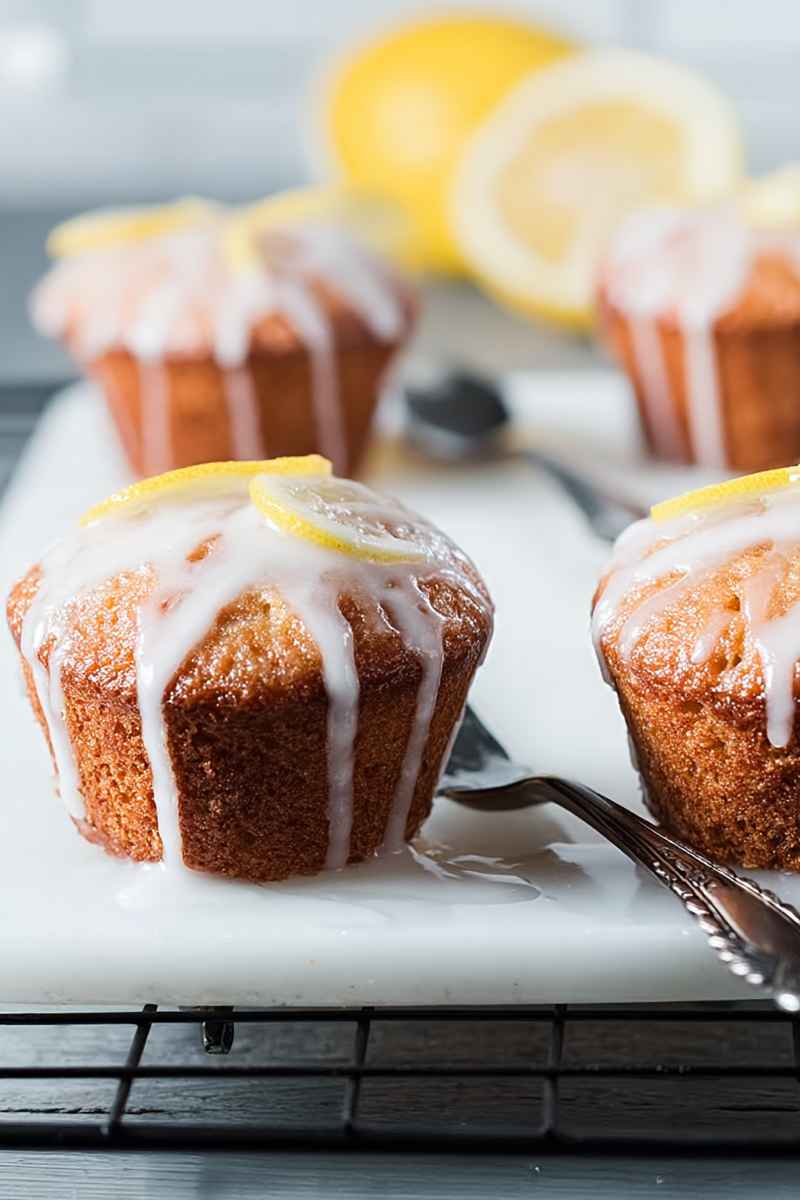 Lemon muffins with a lemon slice garnish, drizzled with glaze, displayed on a white plate with a fork nearby.