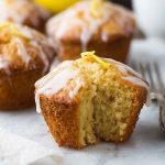 A halved lemon muffin revealing its moist, fluffy texture, topped with a lemon twist and drizzled glaze.
