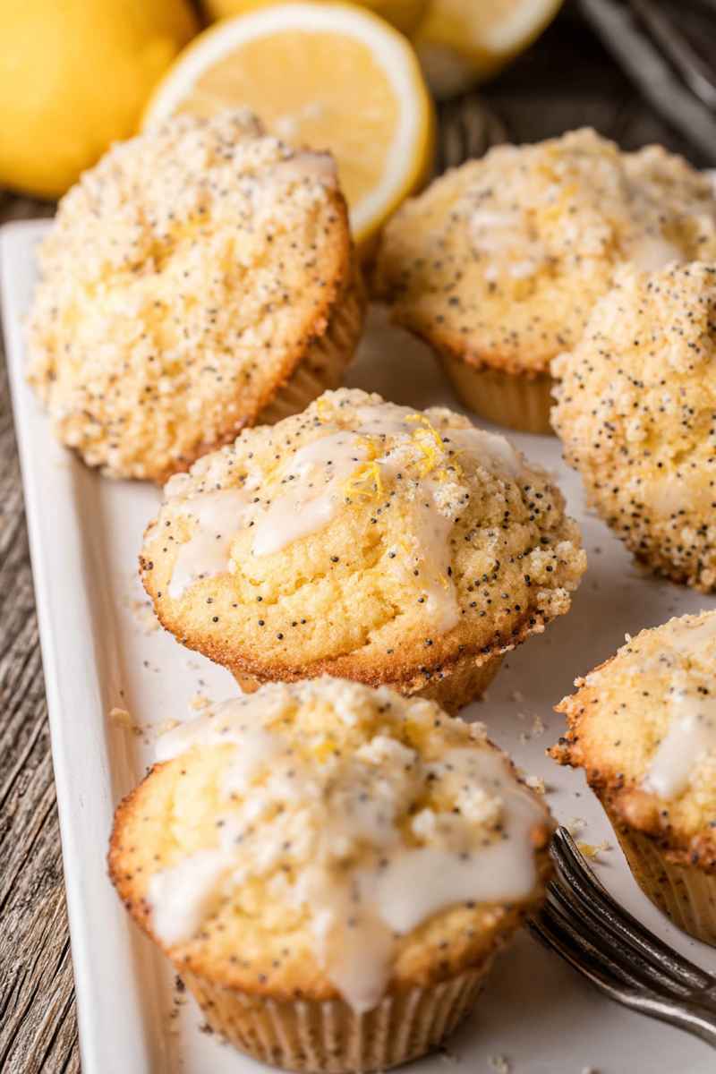 Lemon Poppy Seed Muffins with lemon glaze drizzled over, placed on a white plate with fresh lemons in the background.