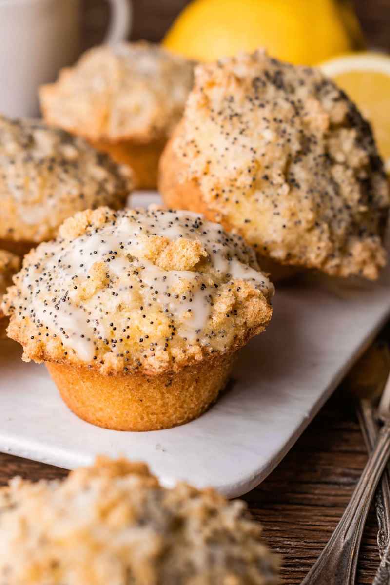 Bright yellow Lemon Poppy Seed Muffins drizzled with lemon glaze, surrounded by fresh lemons.
