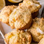 Bright yellow Lemon Poppy Seed Muffins drizzled with lemon glaze, surrounded by fresh lemons.