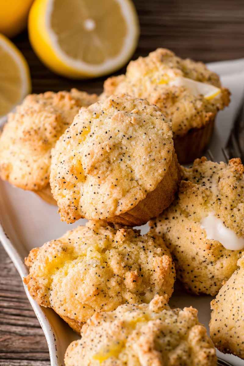Bright yellow Lemon Poppy Seed Muffins drizzled with lemon glaze, surrounded by fresh lemons.