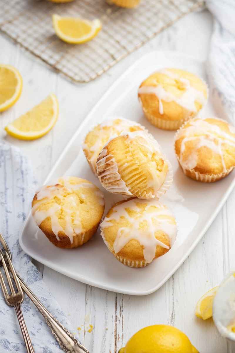 Golden Lemon Pound Cake Muffins with lemon glaze, displayed on a white plate with lemon slices scattered around.