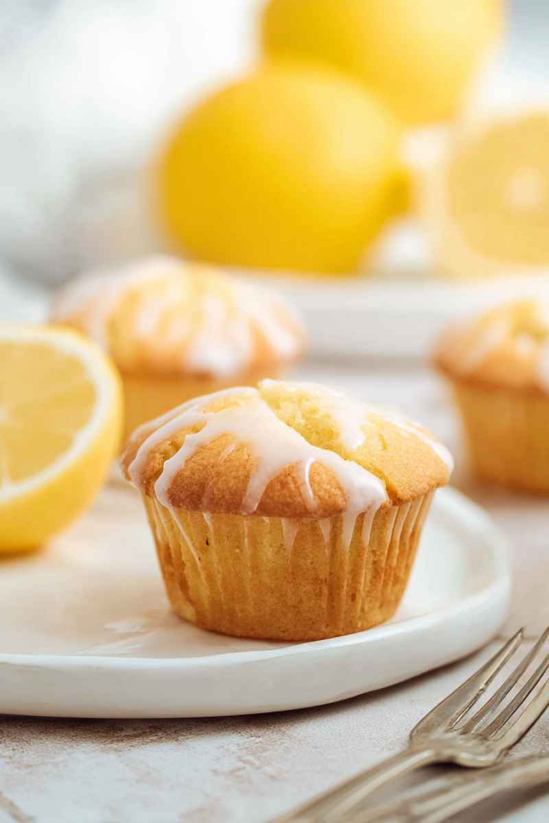 A Lemon Pound Cake Muffin with a drizzle of lemon glaze, served on a white plate with fresh lemons in the background.