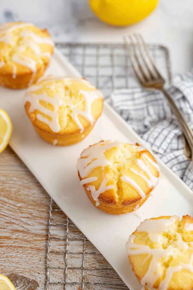 Three Lemon Pound Cake Muffins with a glossy lemon glaze, arranged on a white rectangular plate.