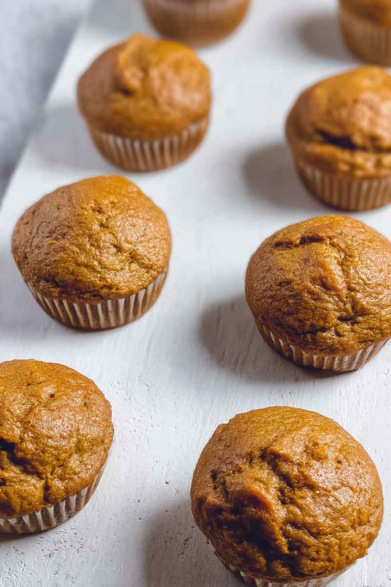 Golden-brown low carb pumpkin protein muffins arranged on a white surface, showcasing their moist texture and warm spices.
