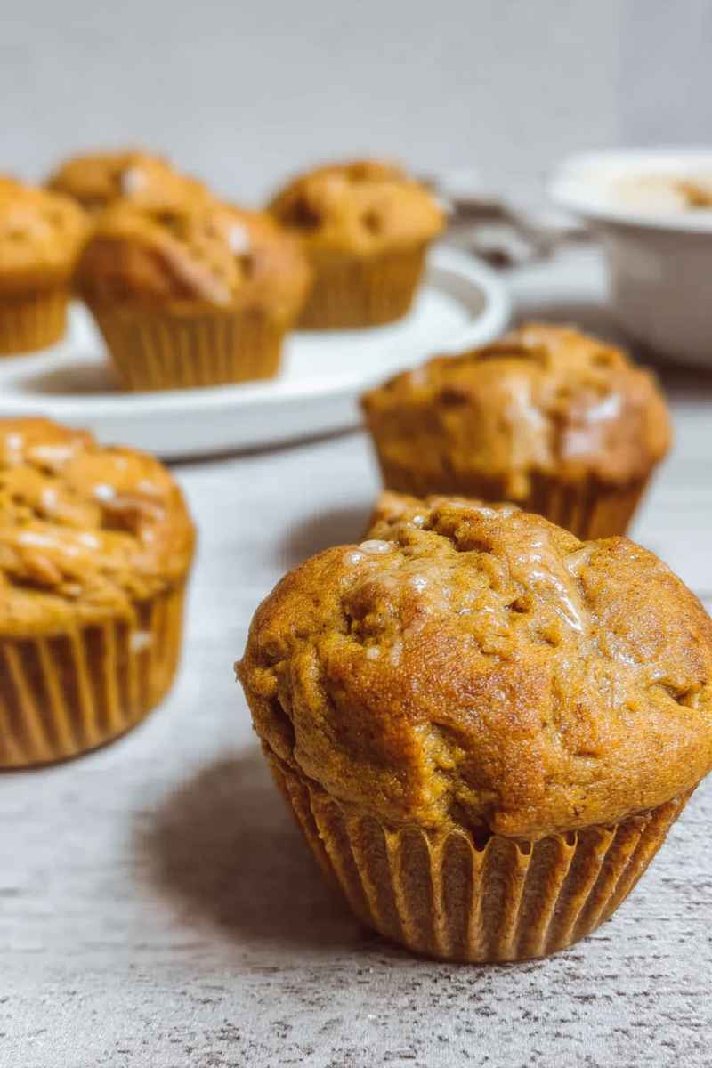 Golden pumpkin protein muffins topped with a glossy glaze, adding a touch of sweetness to their earthy tones.