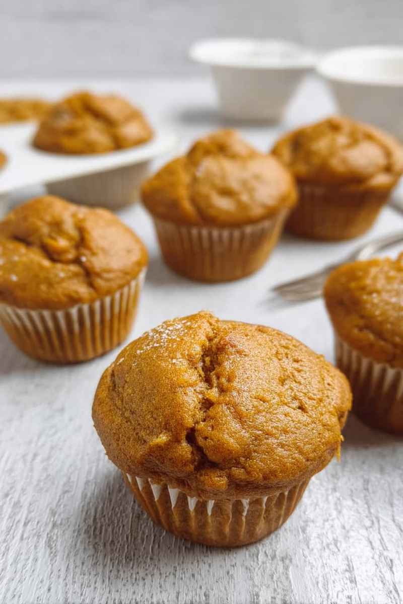 A plate of golden pumpkin protein muffins dusted with powdered sugar, highlighting their homemade appeal.