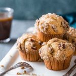 Maple Pecan Muffins with a golden dome and crumb topping, served on a white platter near a glass of coffee.