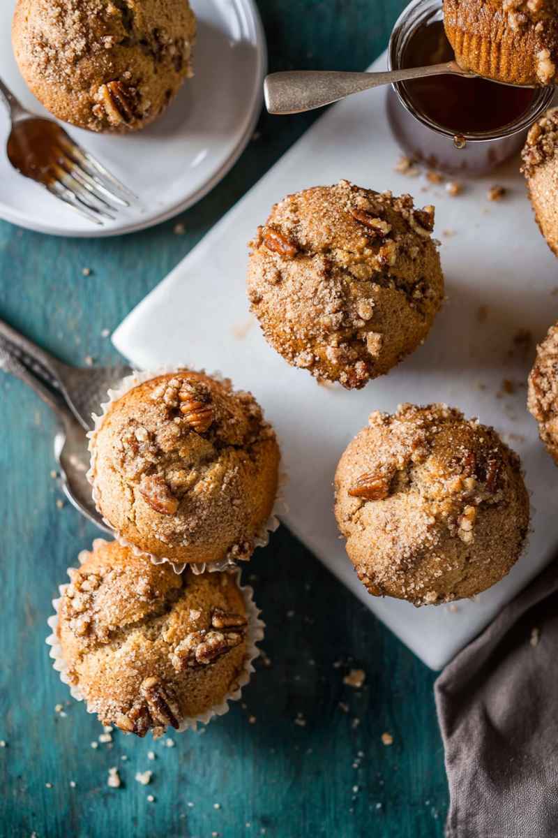 Golden-brown Maple Pecan Muffins with crumbly streusel topping, arranged on a white platter near a cup of coffee.