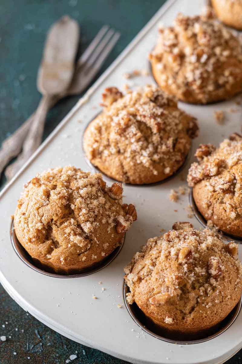 Golden-brown Maple Pecan Muffins topped with crunchy streusel, sitting on a white tray.