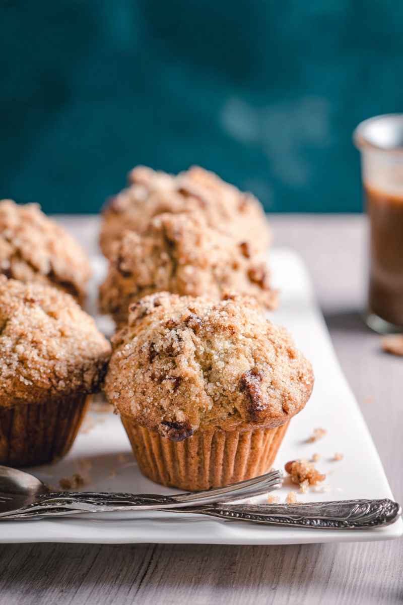 Three Maple Pecan Muffins arranged on a white platter, with a glass of coffee in the background.