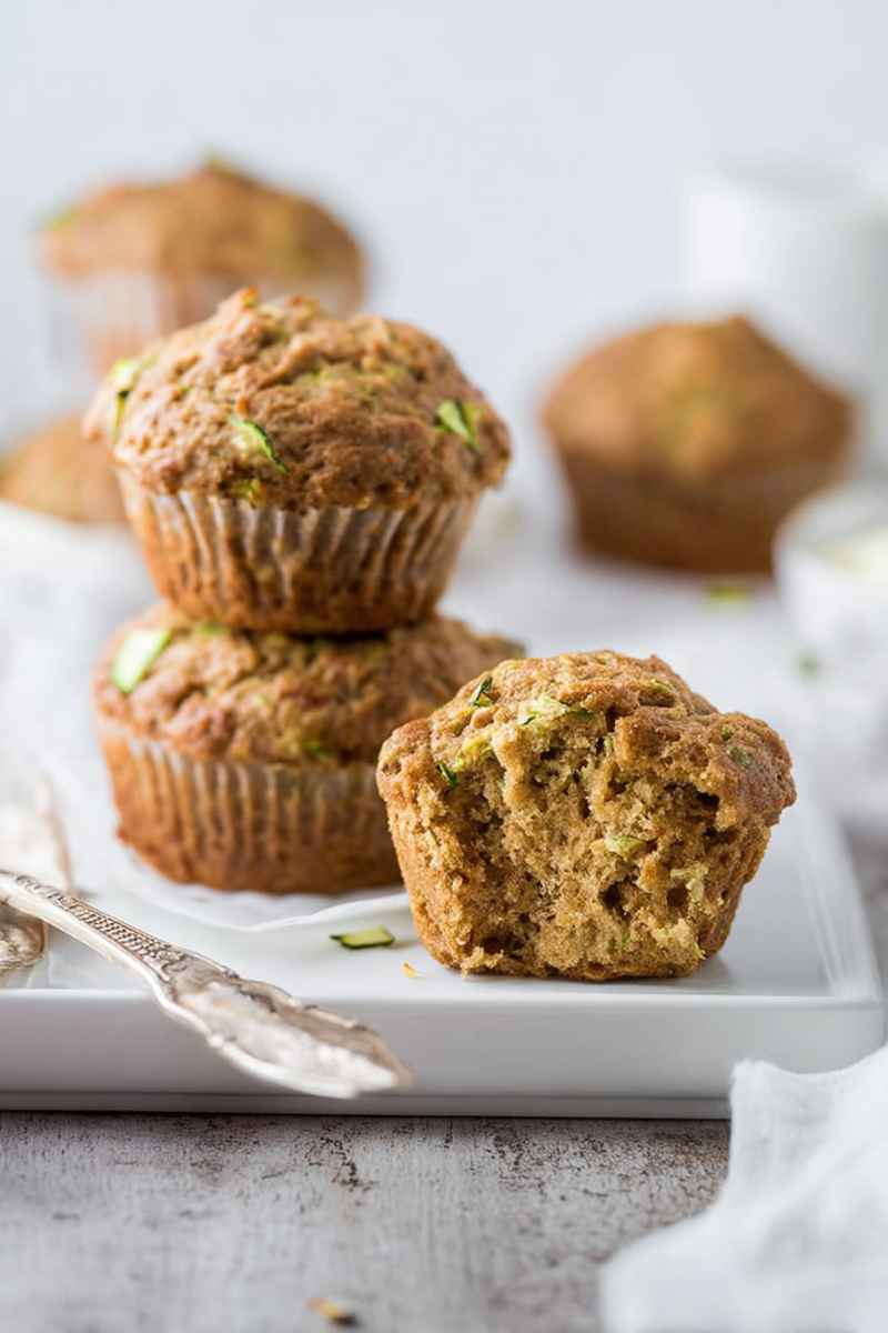 Three zucchini muffins stacked on a white plate, showcasing their golden-brown tops and moist interiors.