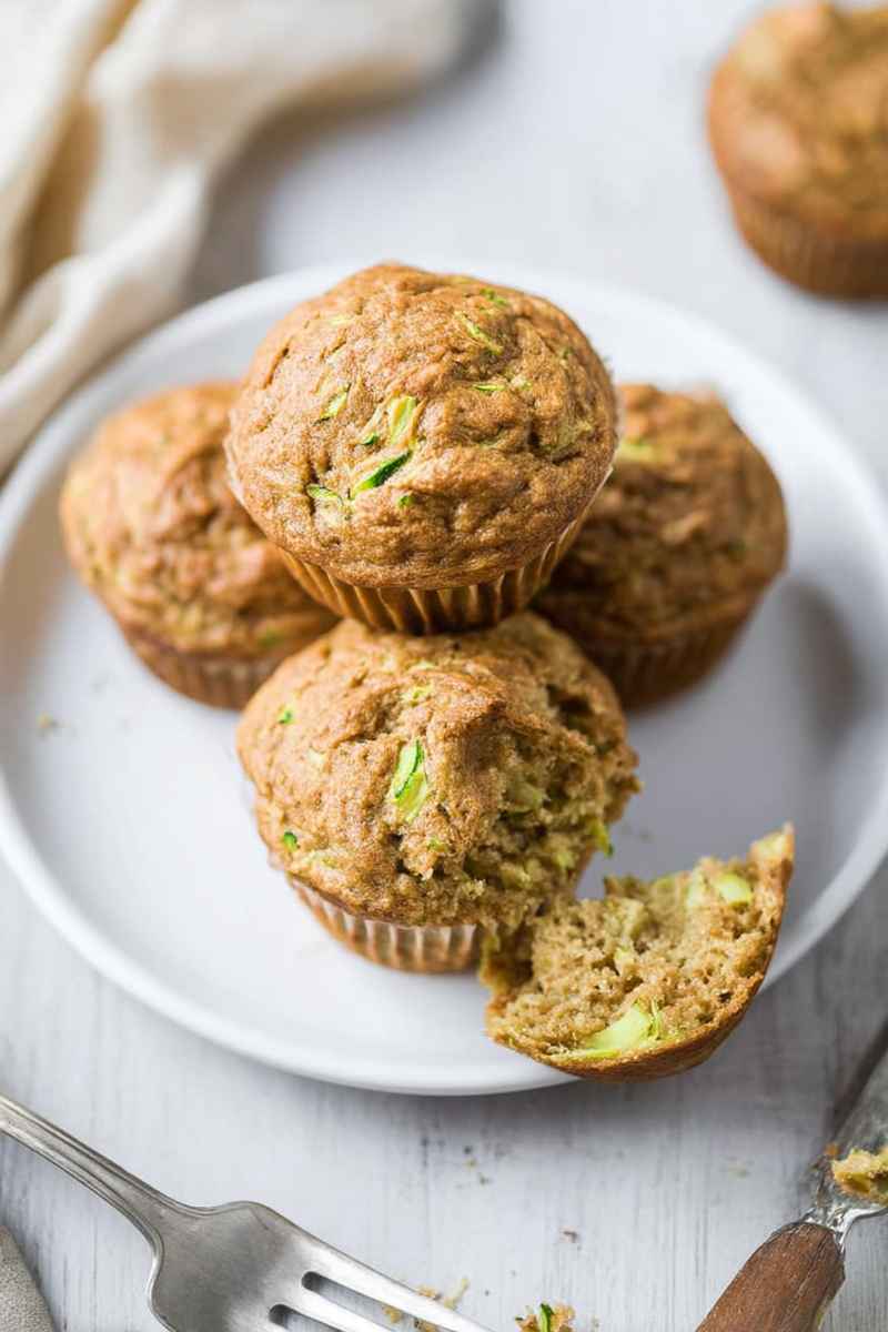 A plate of zucchini muffins, one cut open to show the soft, moist texture inside.